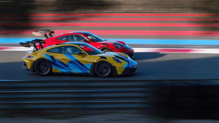 Deux Porsche 911 GT3 type 992, l'une rouge et l'une jaune, en pleine course côte à côte sur le circuit Paul Ricard.